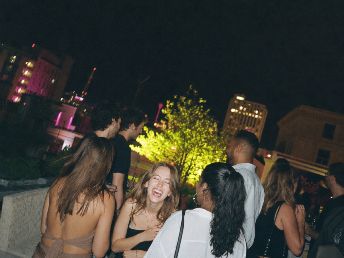 Invitados riendo en una fiesta en la azotea de noche, iluminados por el flash de una cámara